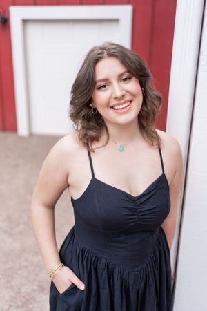 A person in a black dress poses against a red barn wall wearing a turquoise necklace.