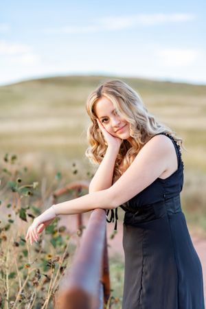 Woman in black dress poses thoughtfully against rolling hills during golden hour.