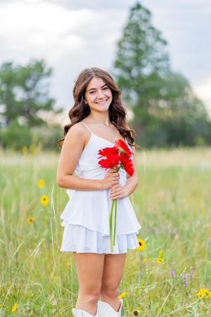 Summer fashion portrait with red gerbera daisies and white dress in meadow setting.