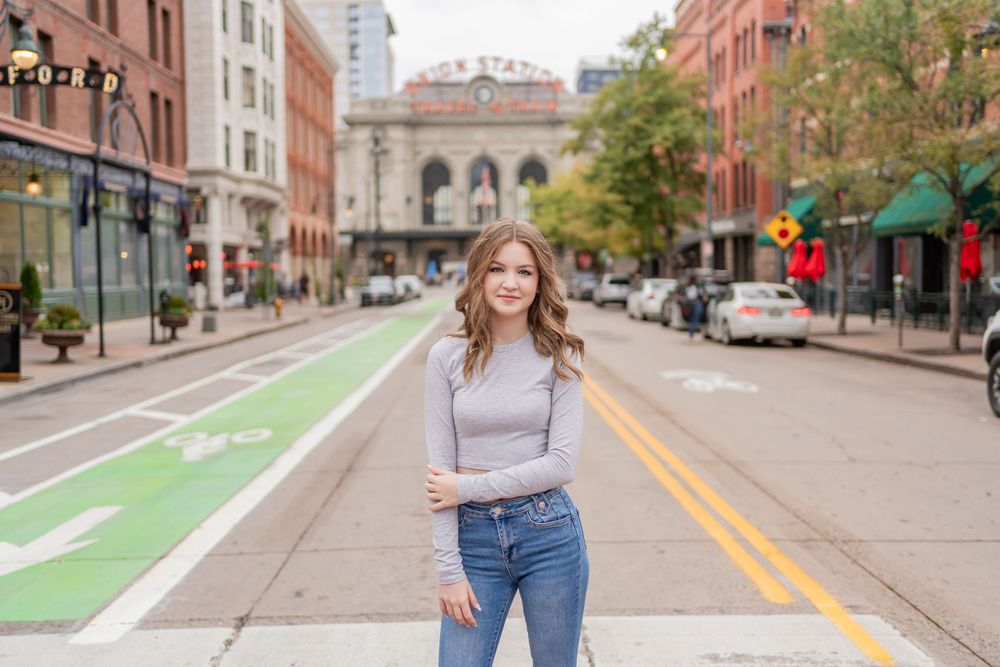 Woman in casual attire poses in middle of city street with historic buildings.