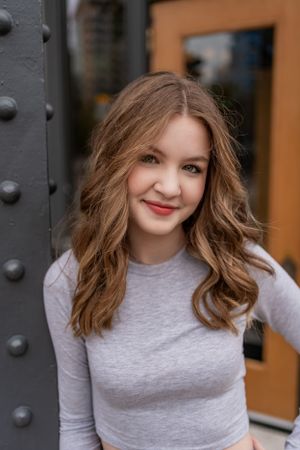 Woman in gray top smiles while standing next to industrial metal column.
