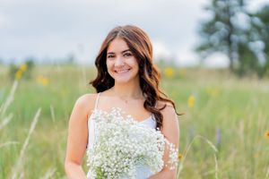 Outdoor portrait in a meadow with baby's breath bouquet against a soft cloudy sky.