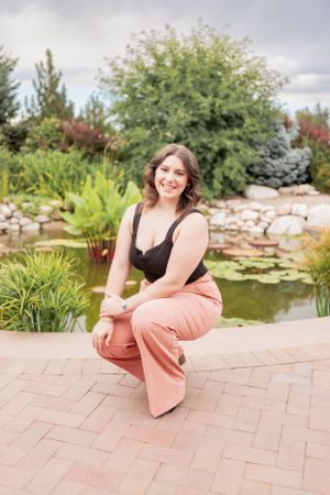 Casual outdoor portrait by a garden pond with pink pants and black top.
