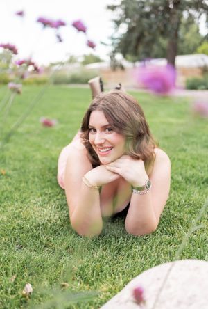 Portrait of a smiling person lying in grass with pink flowers on a sunny day.