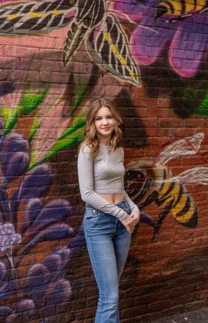 Woman poses in front of colorful floral street art mural on brick wall.