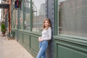 Woman in casual outfit stands against vintage green storefront with industrial details.