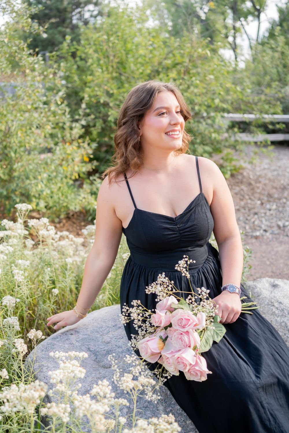 Outdoor portrait with a black dress and pink bouquet against a natural garden backdrop.