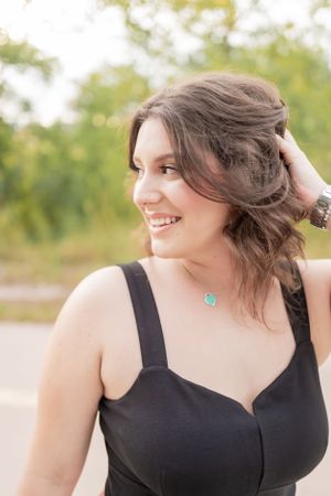 A candid outdoor portrait showing wavy hair, a black dress, and turquoise jewelry.
