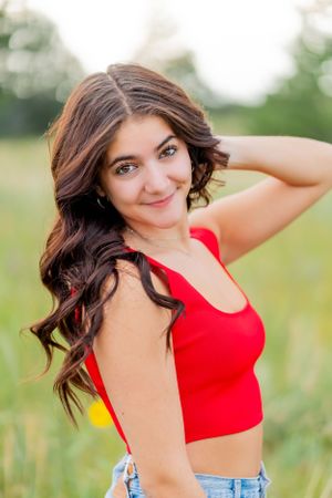 Portrait of woman with wavy hair wearing red tank top in outdoor nature setting.
