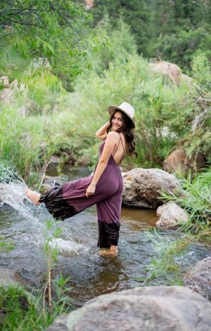 Woman in purple dress splashes in mountain stream among rocks.