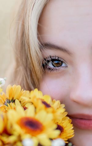 Close-up of a brown eye with yellow daisy flowers in soft focus.
