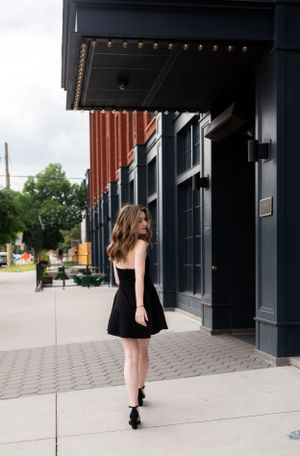 Street style photo in black dress walking past urban storefronts.