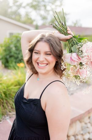 Joyful outdoor portrait holding pink roses in a black sundress.