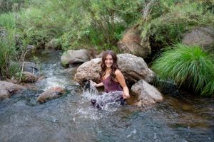 Woman plays in mountain creek creating water splashes among rocks.