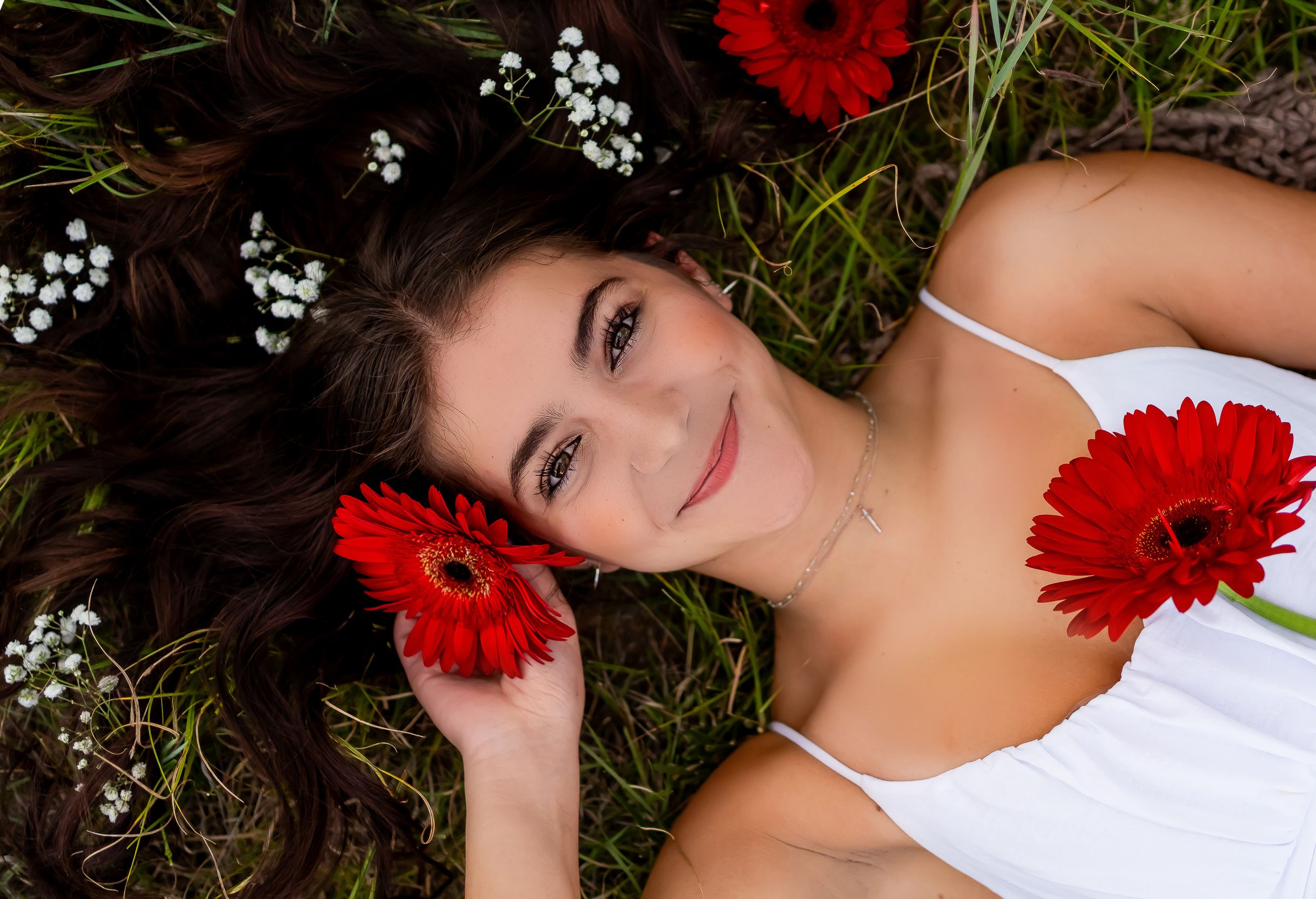 Artistic overhead portrait with red flowers and baby's breath in hair while laying in grass.