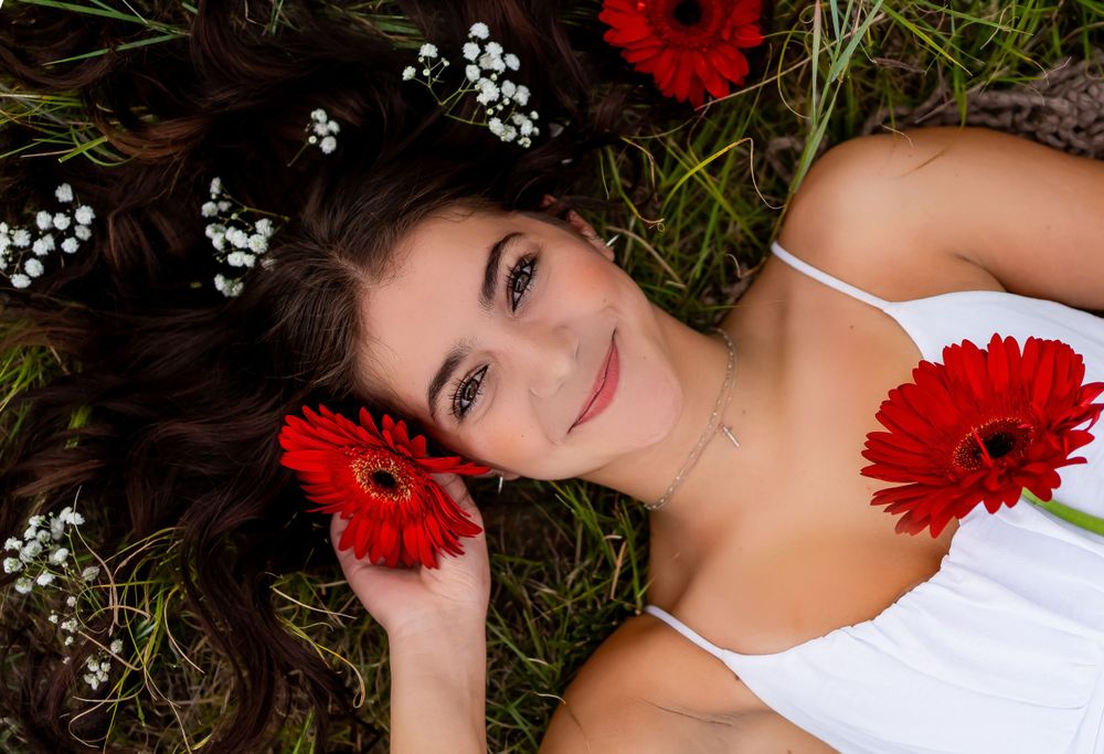 Artistic overhead portrait with red flowers and baby's breath in hair while laying in grass.