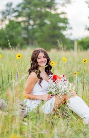 Casual summer portrait sitting in wildflower field with bouquet and white boots.
