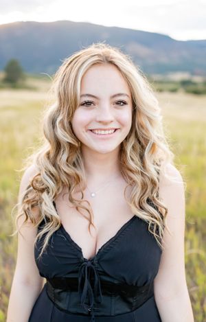 Portrait in black dress against mountain backdrop with wavy blonde hair.
