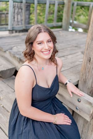 Portrait on a wooden deck wearing a navy dress and delicate jewelry.