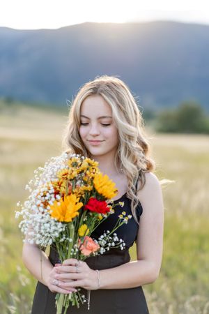 Holding colorful wildflower bouquet with sunflowers and baby's breath in meadow.