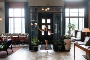 Elegant lobby interior with dark walls, high windows, ornate decor and potted plants framing an entrance.