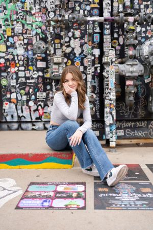 Casual portrait against colorful sticker-covered wall with street art background.