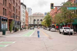 Person walking down urban street with historic architecture and green bike lane.