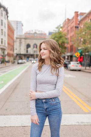 Woman stands on urban street with historic architecture and bike lane visible.