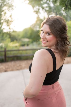 Portrait with black top and pink pants in outdoor garden setting.
