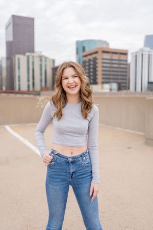 Casual urban portrait featuring a gray crop top and jeans against a city skyline background.