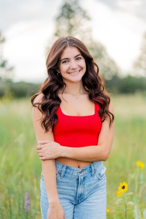 Young woman in red crop top and jeans poses in a wildflower meadow at sunset.
