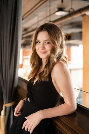 Artistic portrait by a window showcasing a black dress against moody interior lighting.