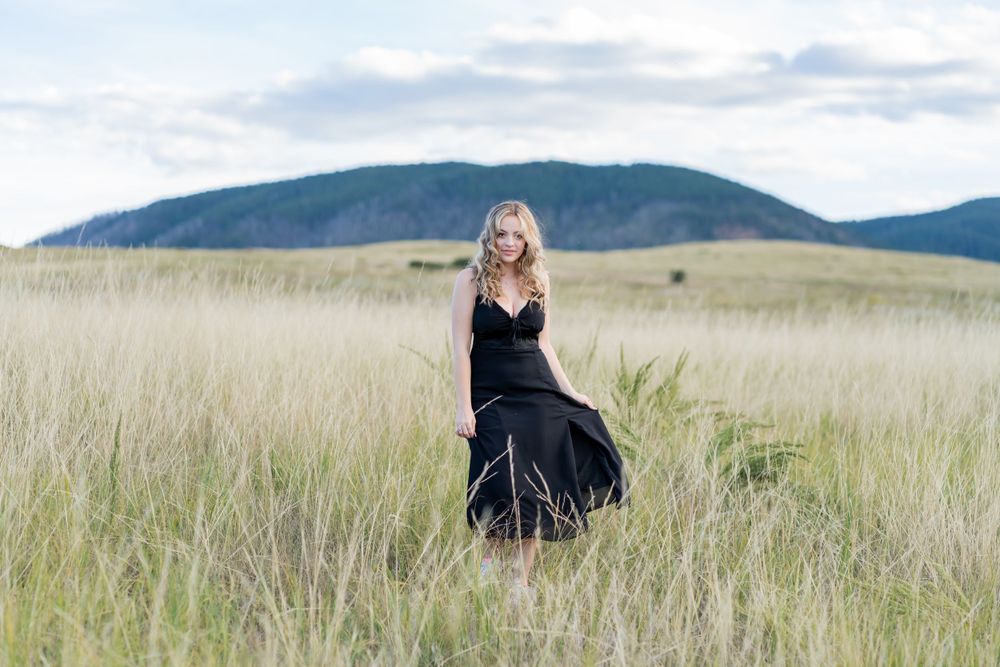 Black dress flowing in the breeze while standing in a mountain meadow field.