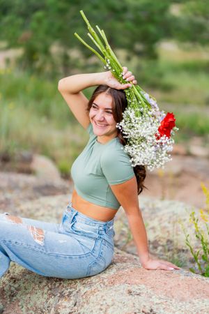 Woman holds bouquet of baby's breath and red flowers while sitting on rocky terrain.