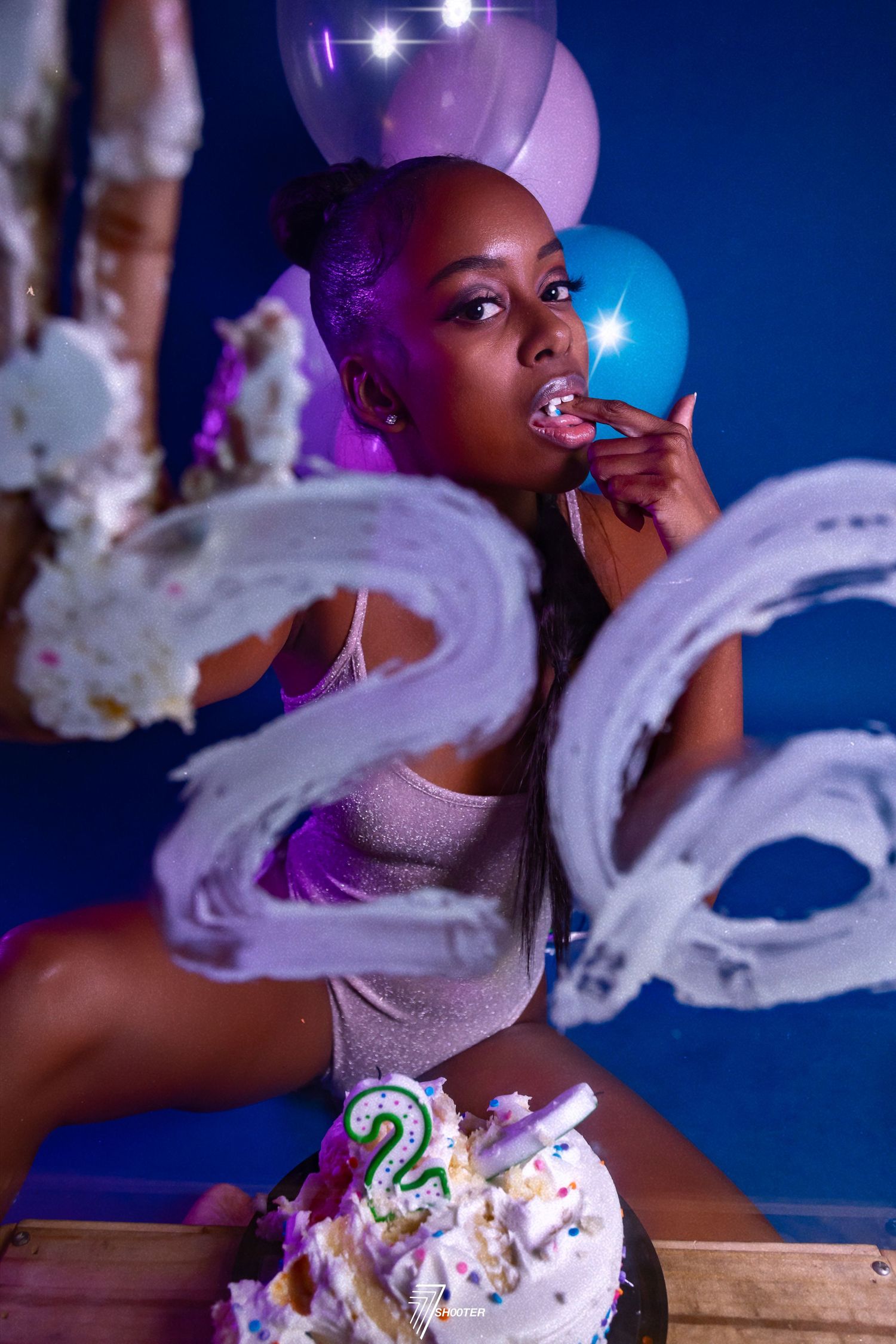A glamorous birthday celebration scene with balloons, cake and sparkles in purple and blue lighting.