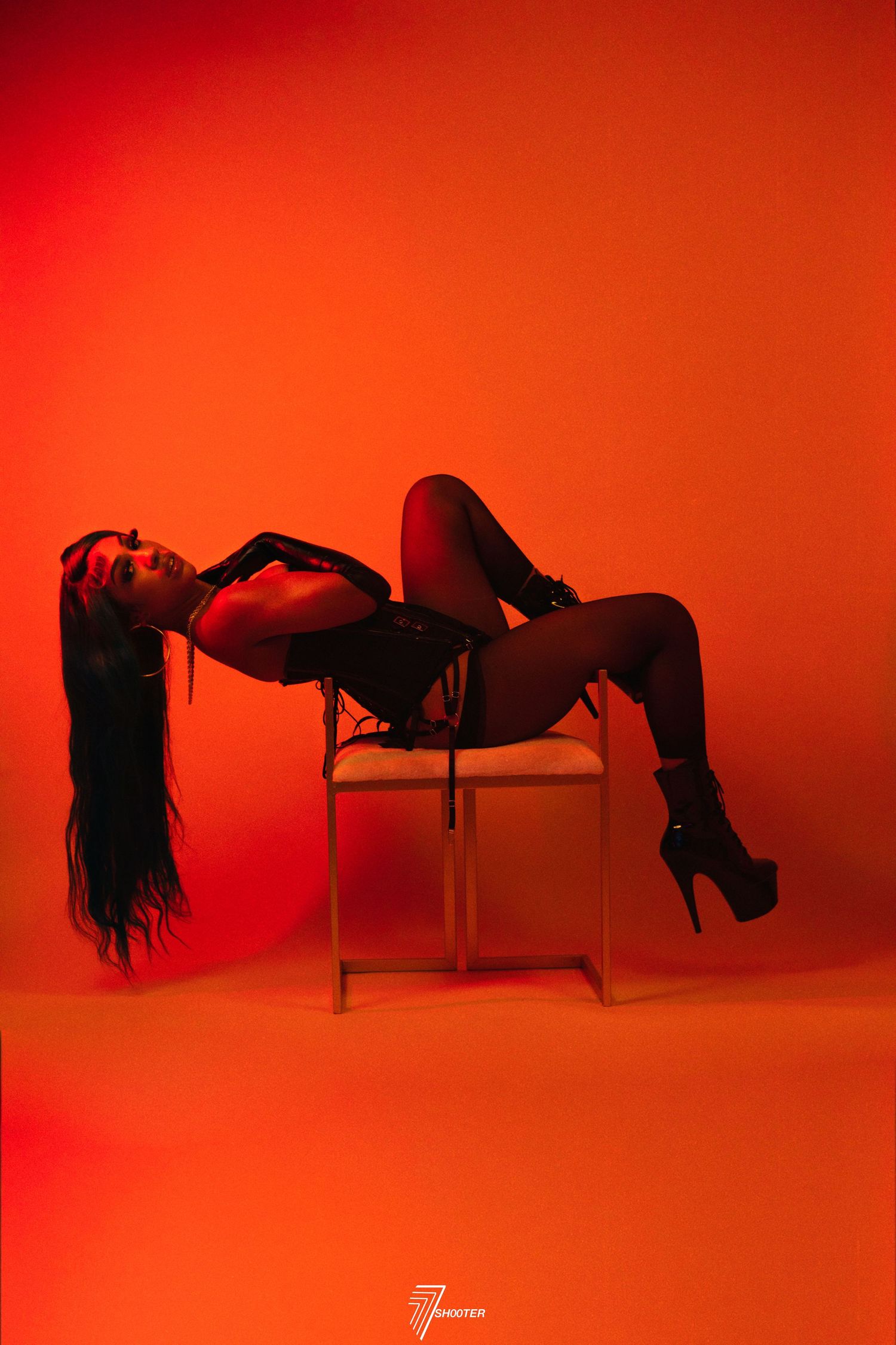 Artistic silhouette photograph of a person posing dramatically on a chair against a vibrant red background.