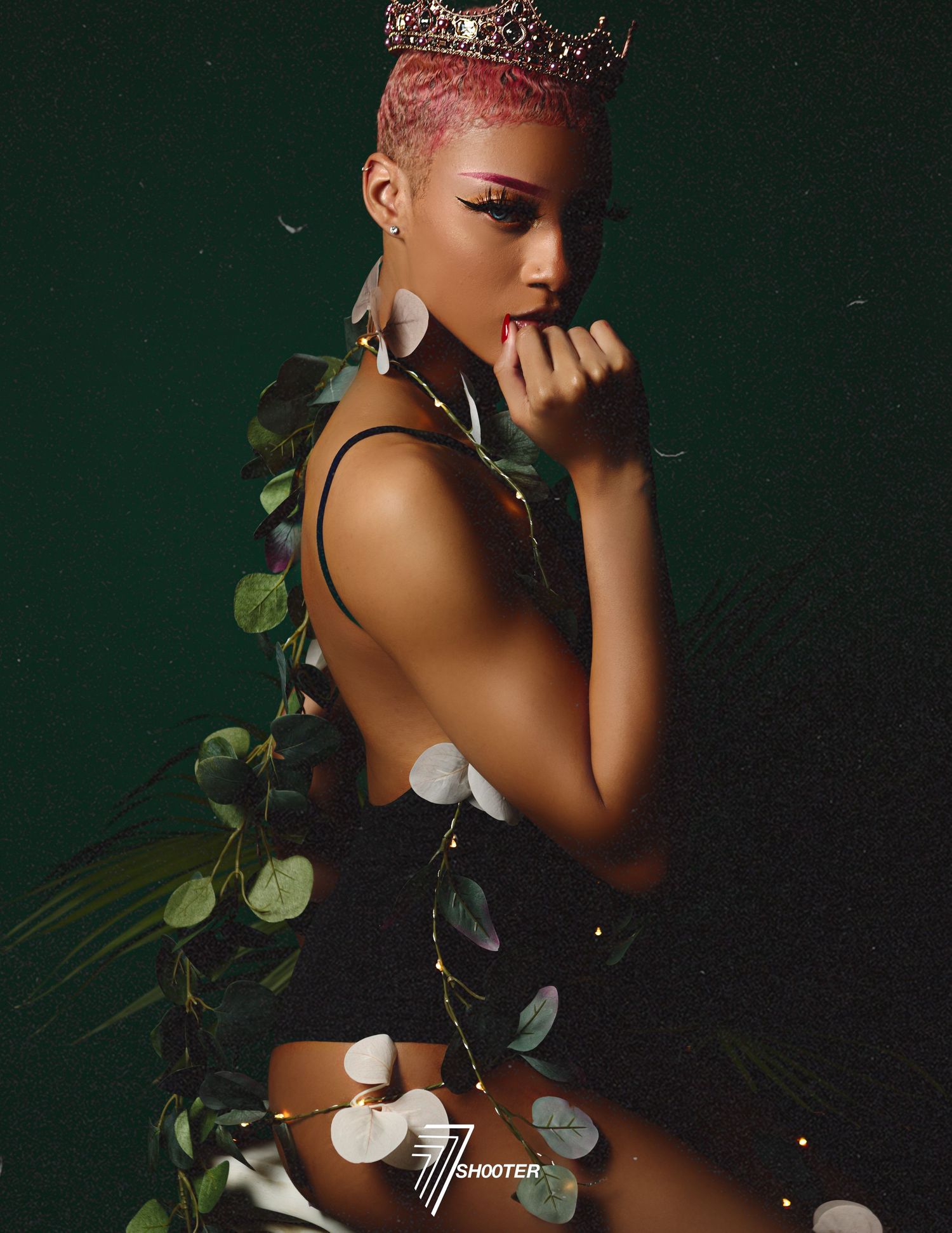 Artistic portrait against dark green background with crown and floral elements wrapped around figure in black attire.