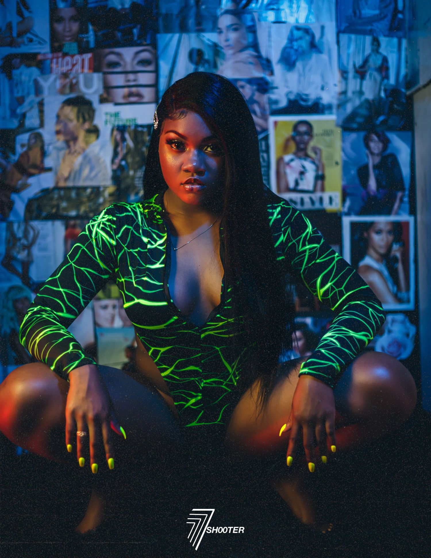 Portrait in a neon green patterned outfit against a wall of vintage photos in moody blue lighting.