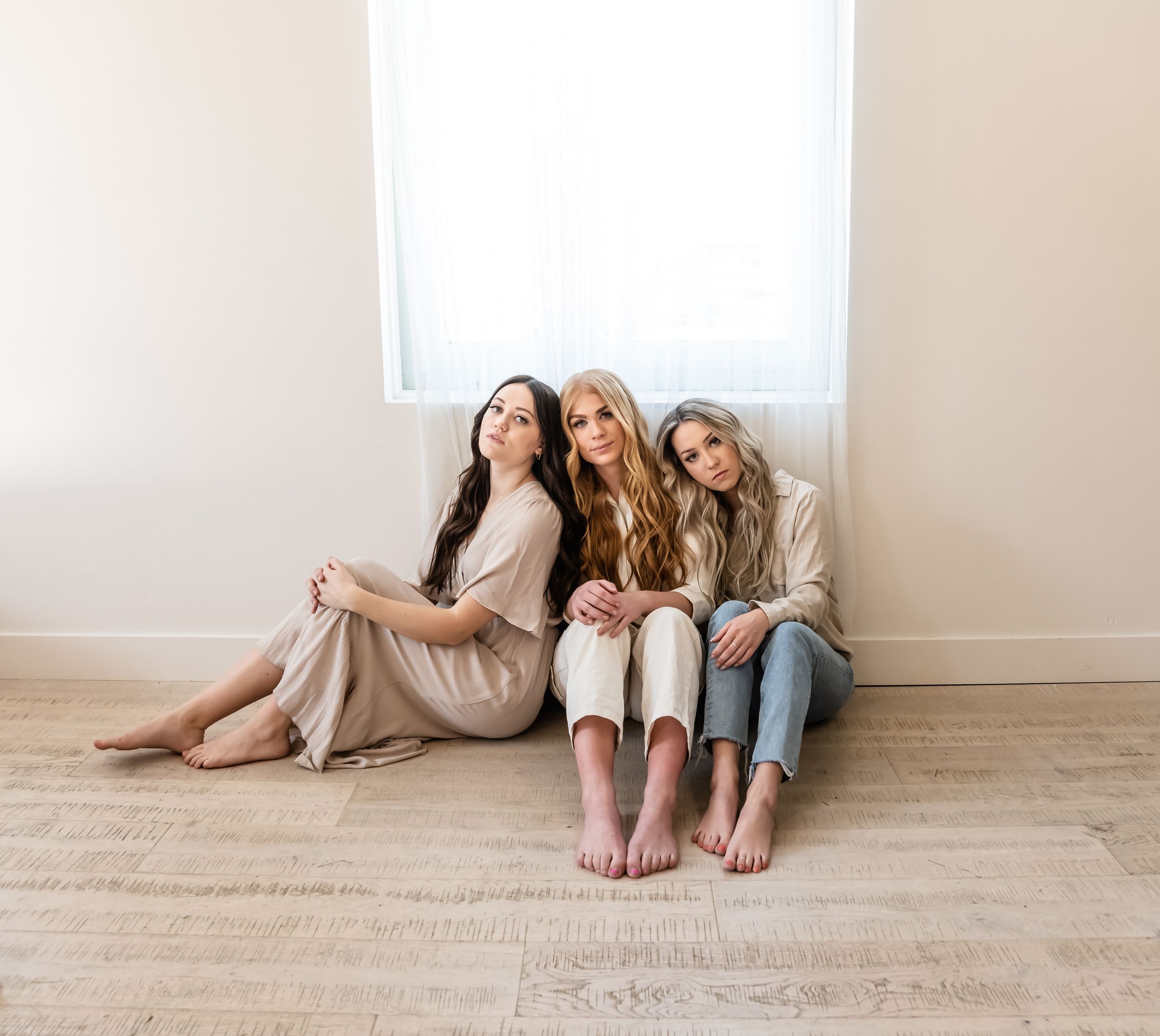 Group relaxing on light wooden flooring against white wall in casual attire.