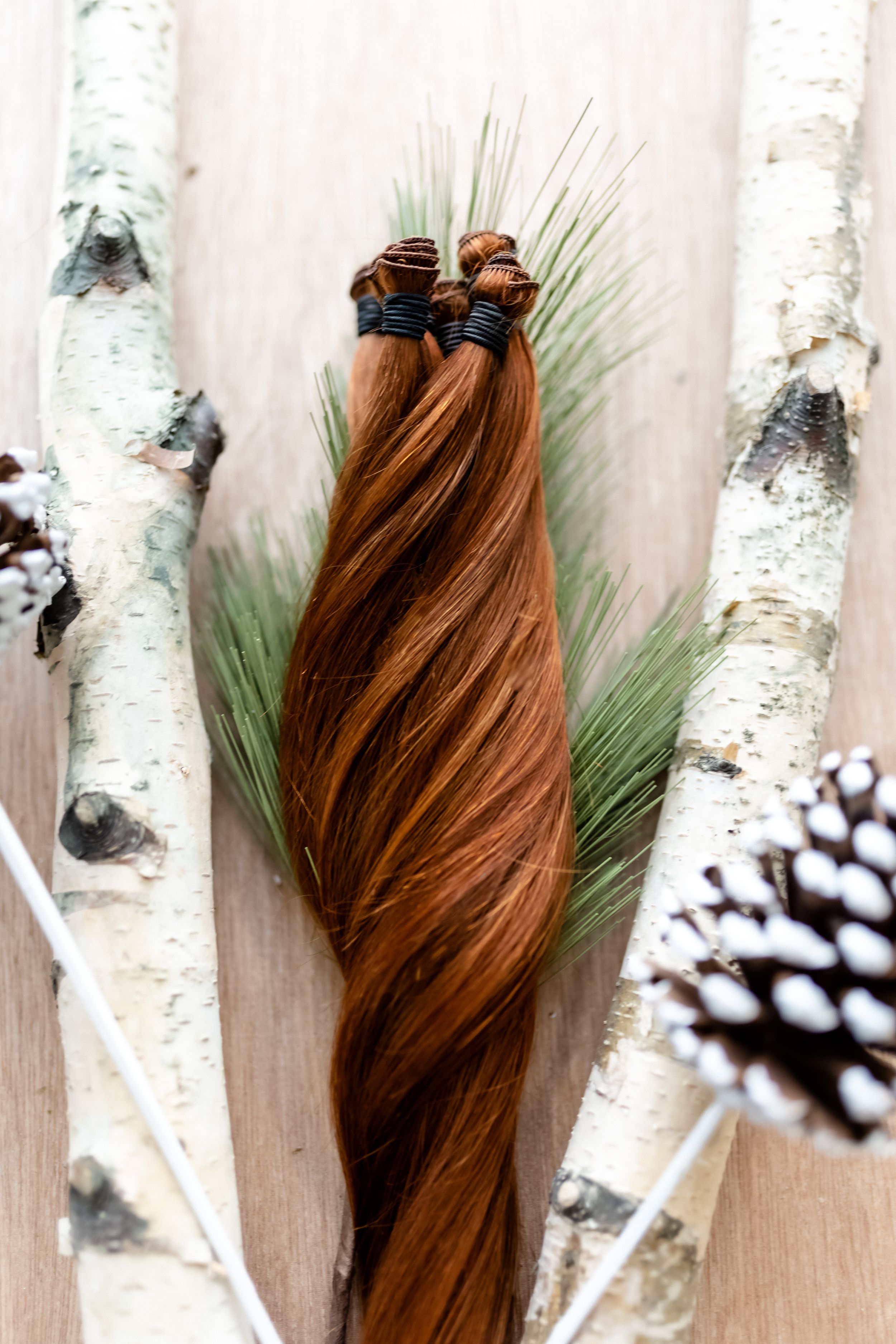 Auburn hair extensions displayed with pine branches and birch bark.