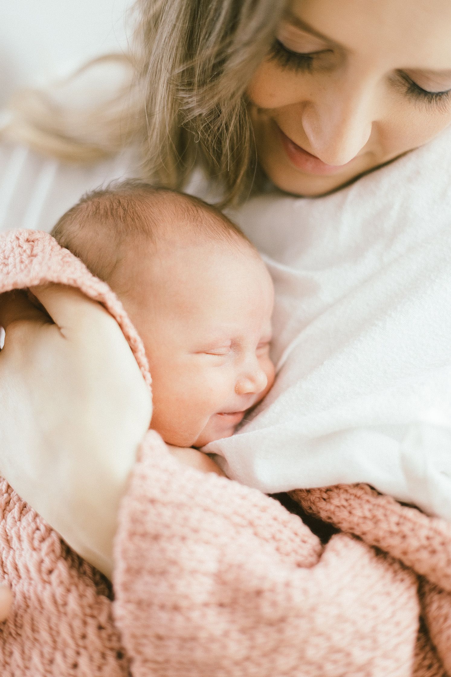 Peaceful moment as sleeping newborn in pink knit blanket rests against caregiver.