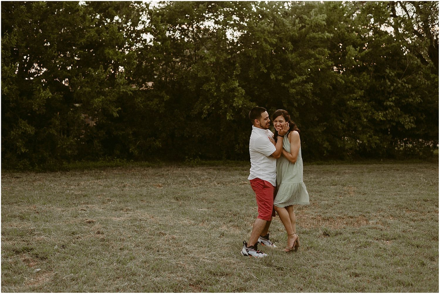 A couple dancing together in a field during sunset.