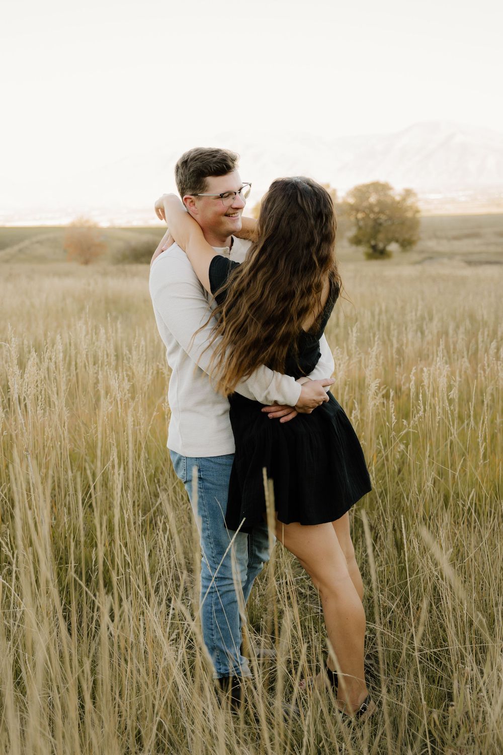 Couple embracing in golden field during sunset photoshoot.