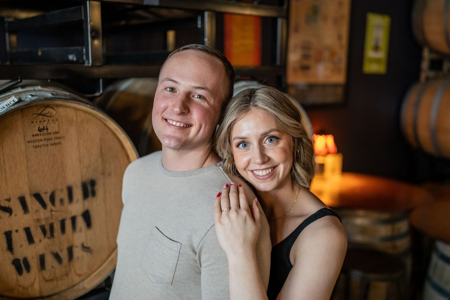 Engaged couple posing together in rustic wine cellar with wooden barrels.