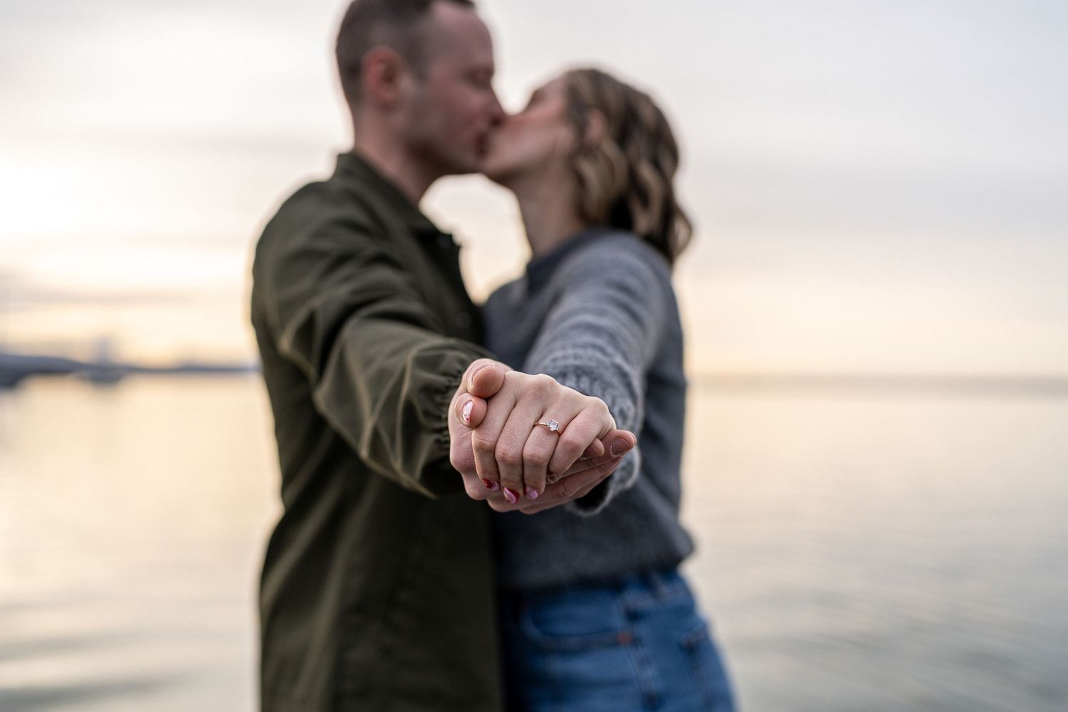 Romantic embrace at sunset with hands clasped in foreground near waterfront.