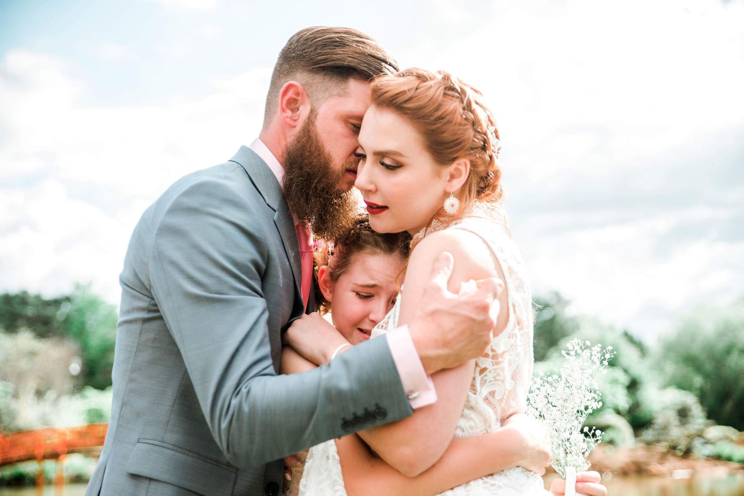 Intimate wedding moment captured in natural light with lace dress and grey suit under cloudy sky.