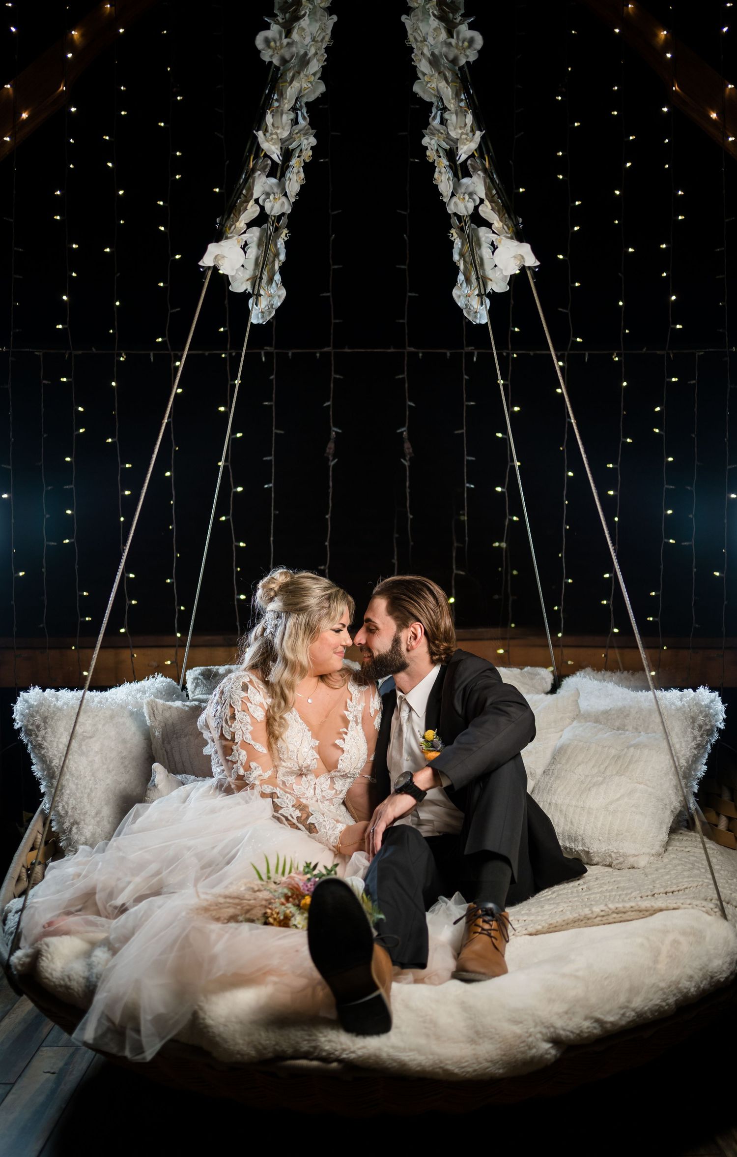 Couple shares intimate moment on suspended swing bed under twinkling lights.