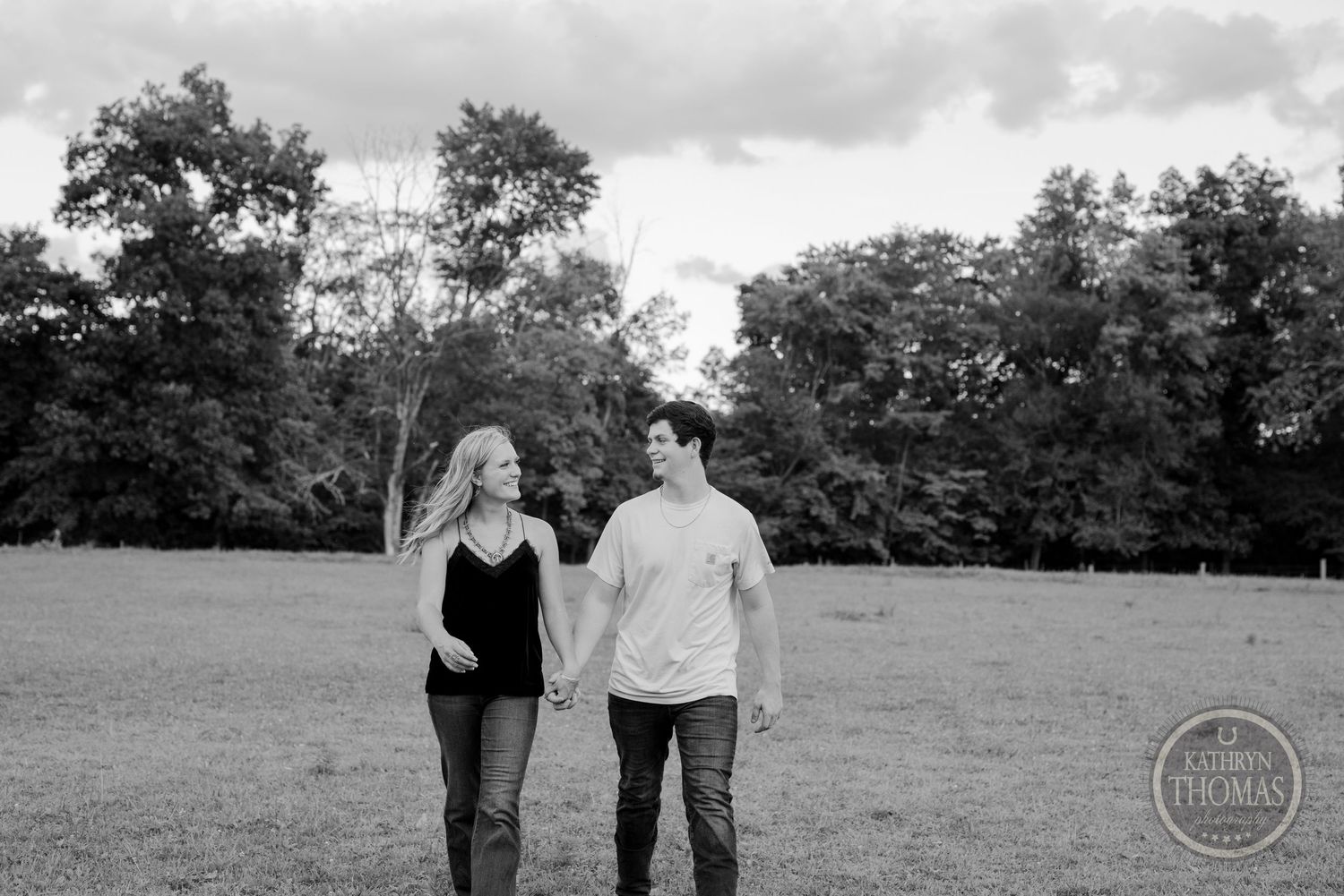 Black and white photo of couple walking together in open field.