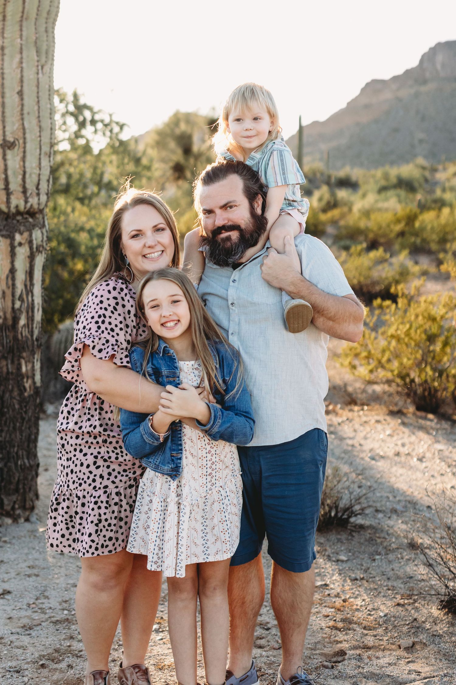 Family portrait session among desert cacti and mountains at sunset.
