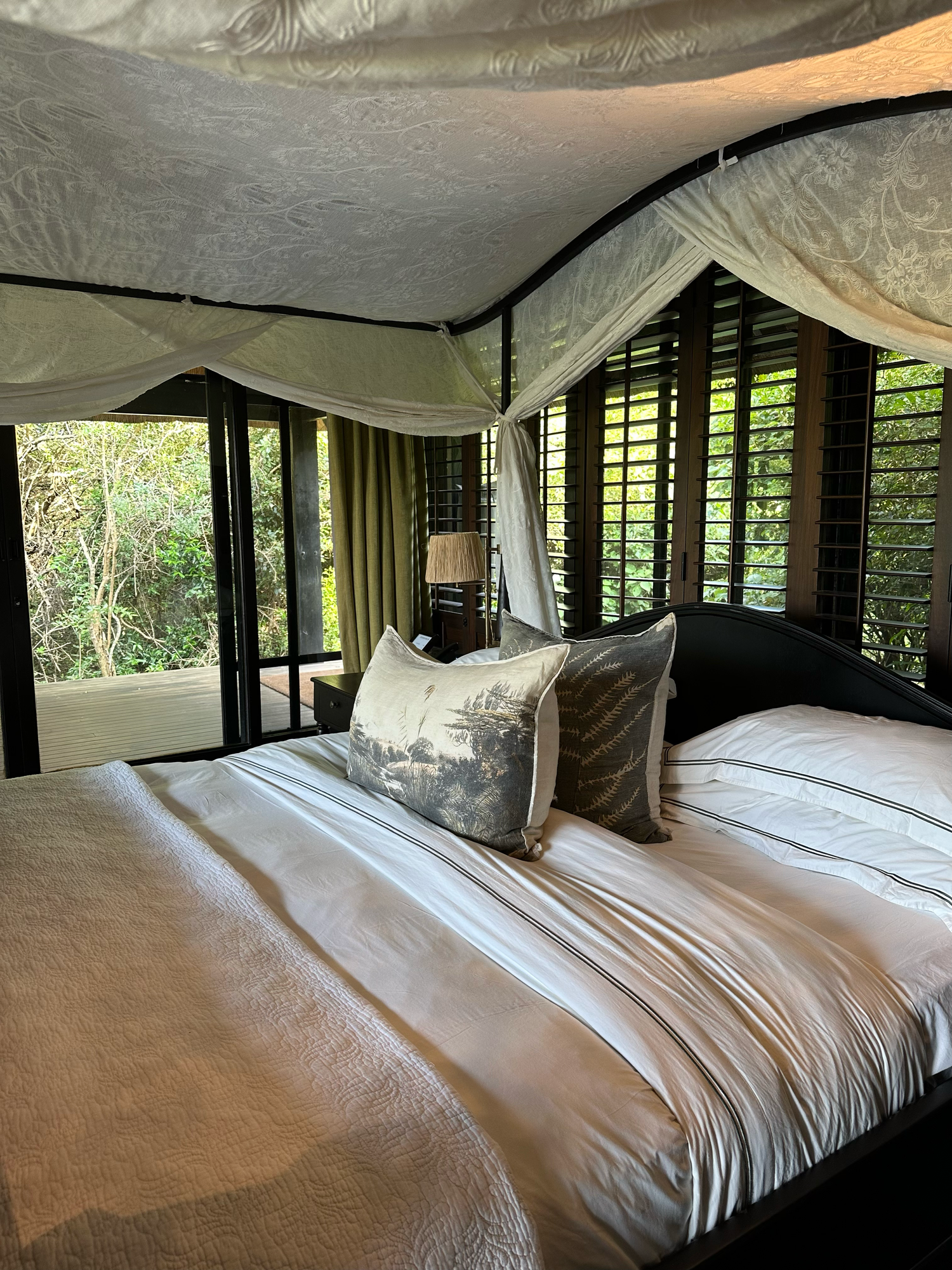 A elegant safari tent bedroom with white linens, draped canvas ceiling, and large windows overlooking nature.